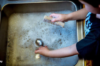 alt="a boy washing utensils in kitchen sink"