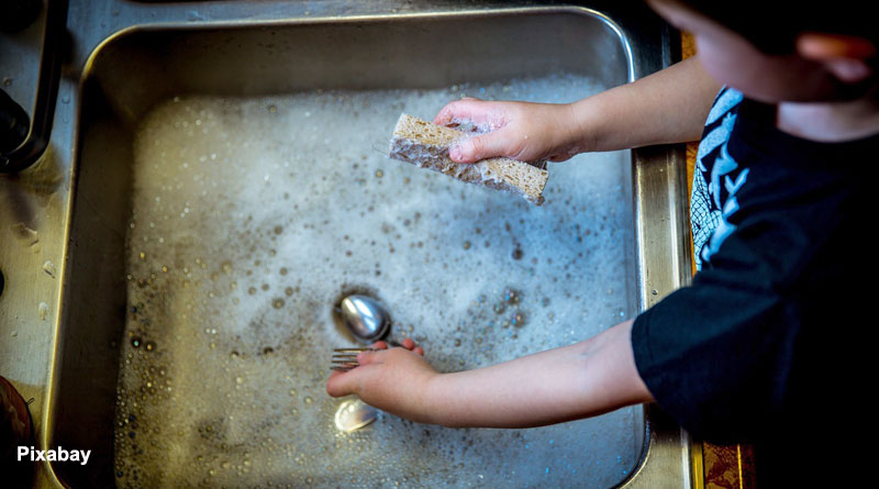 alt="a boy washing utensils in kitchen sink"